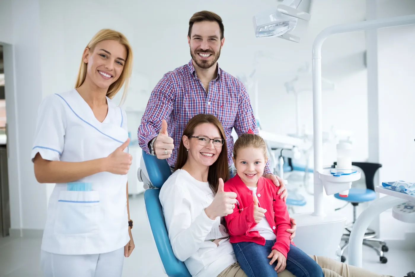 Happy family with child giving thumbs up at the dentist